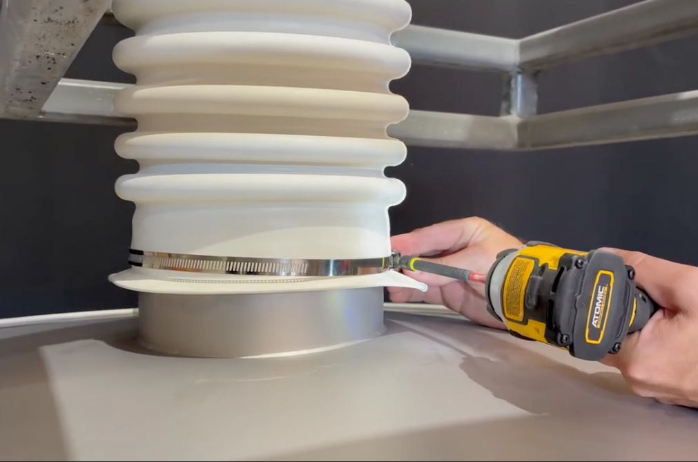 Operator using a power tool to fasten the clamp around the connector boot onto a machine outspout